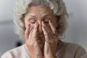 Woman in her 60s rubs her eyes, suffering from dry eye disease.