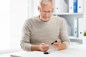 Older man with diabetes checks his blood sugar in his kitchen